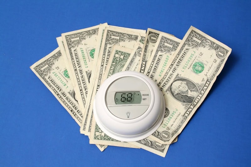 Spring Money-Saving Tips. A thermostat sitting on a pile of money.
