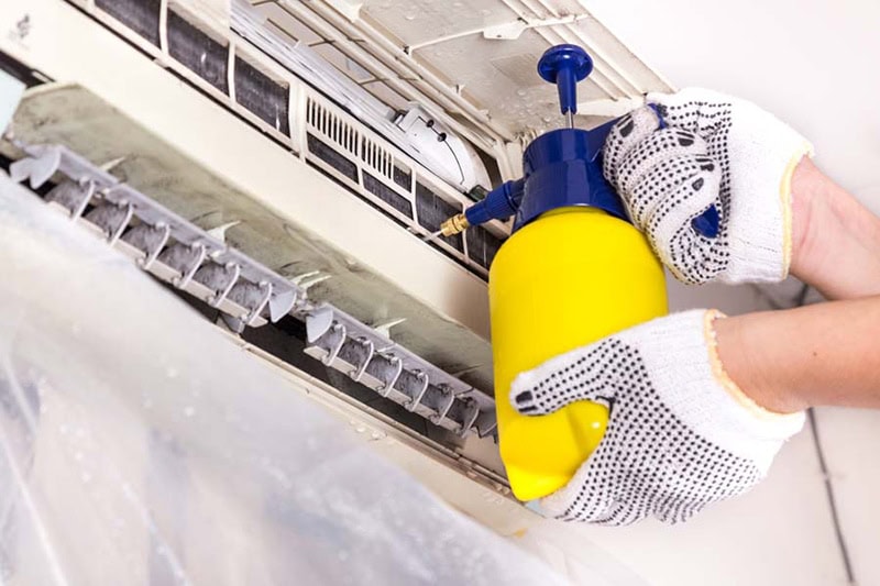 Technician spraying chemical water onto air conditioner grid to clean.