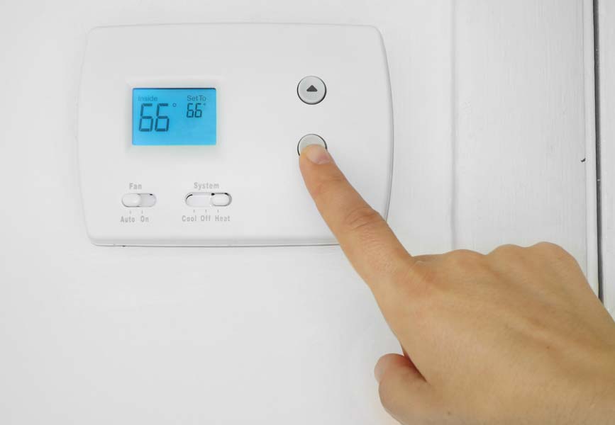 Person's hand adjusting a wall mounted thermostat temperature.