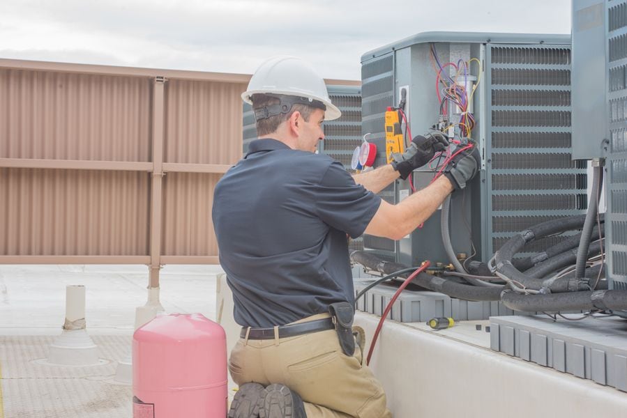 Image of technician working on AC unit. Why Schedule Air Conditioning Maintenance?