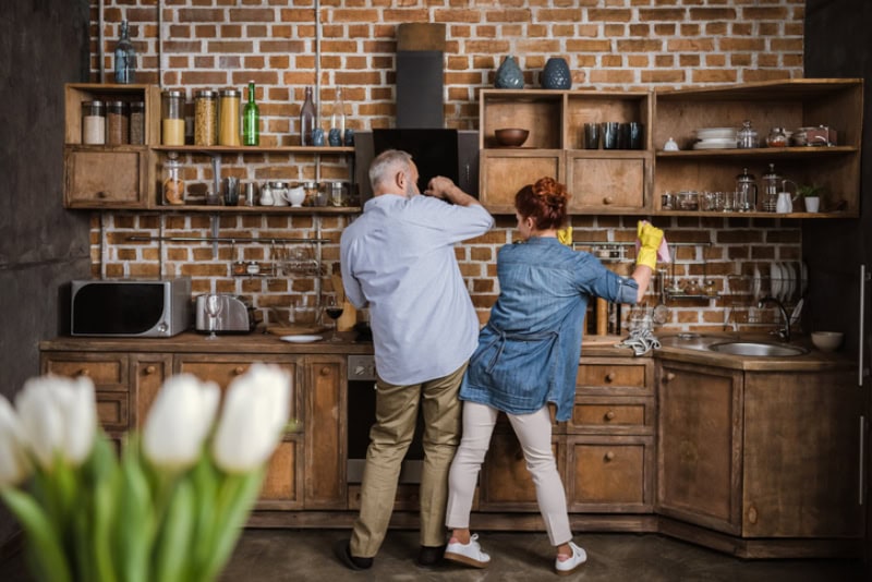 How a Whole-House Humidifier Keeps You Healthy. Back view of mature couple having fun while washing dishes in kitchen.