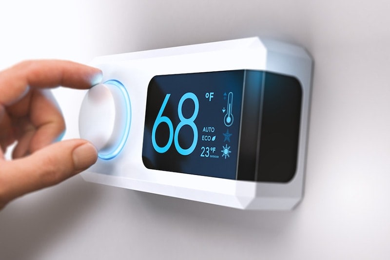 Homeowner adjusting thermostat to HVAC system with AI capabilities.