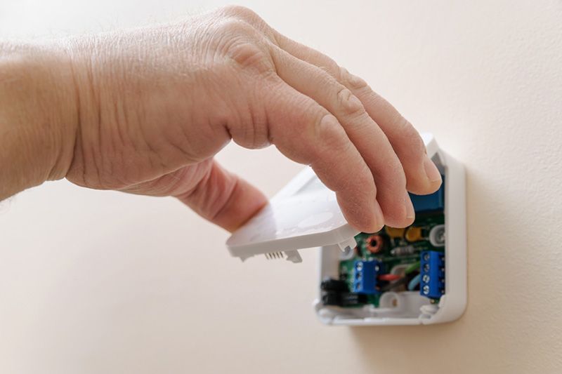 Image of someone pulling the front panel off a thermostat. Tips to Troubleshoot Your Thermostat.